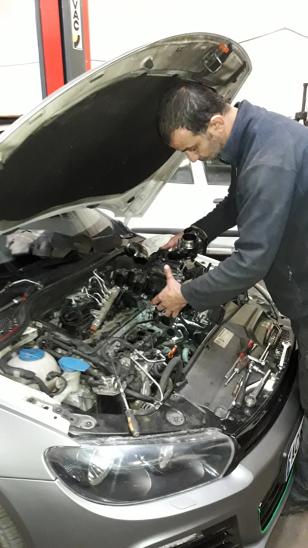 Mécanicien du garage Auto Express penché sur un moteur, capot ouvert, à Marseille